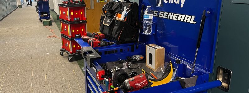 Verkada Installers A school hallway with tool carts, toolboxes, and equipment, including a blue tool chest labeled Jendy and a Milwaukee tool bag. The area appears to be set up for maintenance or repairs.